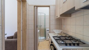 A compact kitchen with a gas stove, a glass shower enclosure, and a beige tiled backsplash.