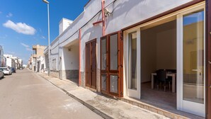 A street view of a building with a covered outdoor seating area and a visible interior space with a table and chairs.