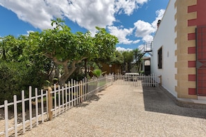 A gravel pathway leading to a building with a white and red facade, surrounded by greenery and a white fence.