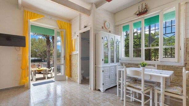 A room with a tiled floor, a white table with chairs, a cabinet with glass doors, and a window with a ship decoration. - 1960 Villa Aurora - Mono Aury by Barbarhouse (Porto Cesareo)