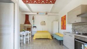 A compact room with a bed, a small table with chairs, a kitchenette, and a door leading to another room. - 1960 Villa Aurora - Mono Aury by Barbarhouse (Porto Cesareo)