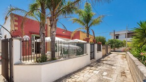 A paved pathway flanked by a white wall and a black metal fence, leading to a building with a red roof. - 1960 Villa Aurora - Mono Aury by Barbarhouse (Porto Cesareo)