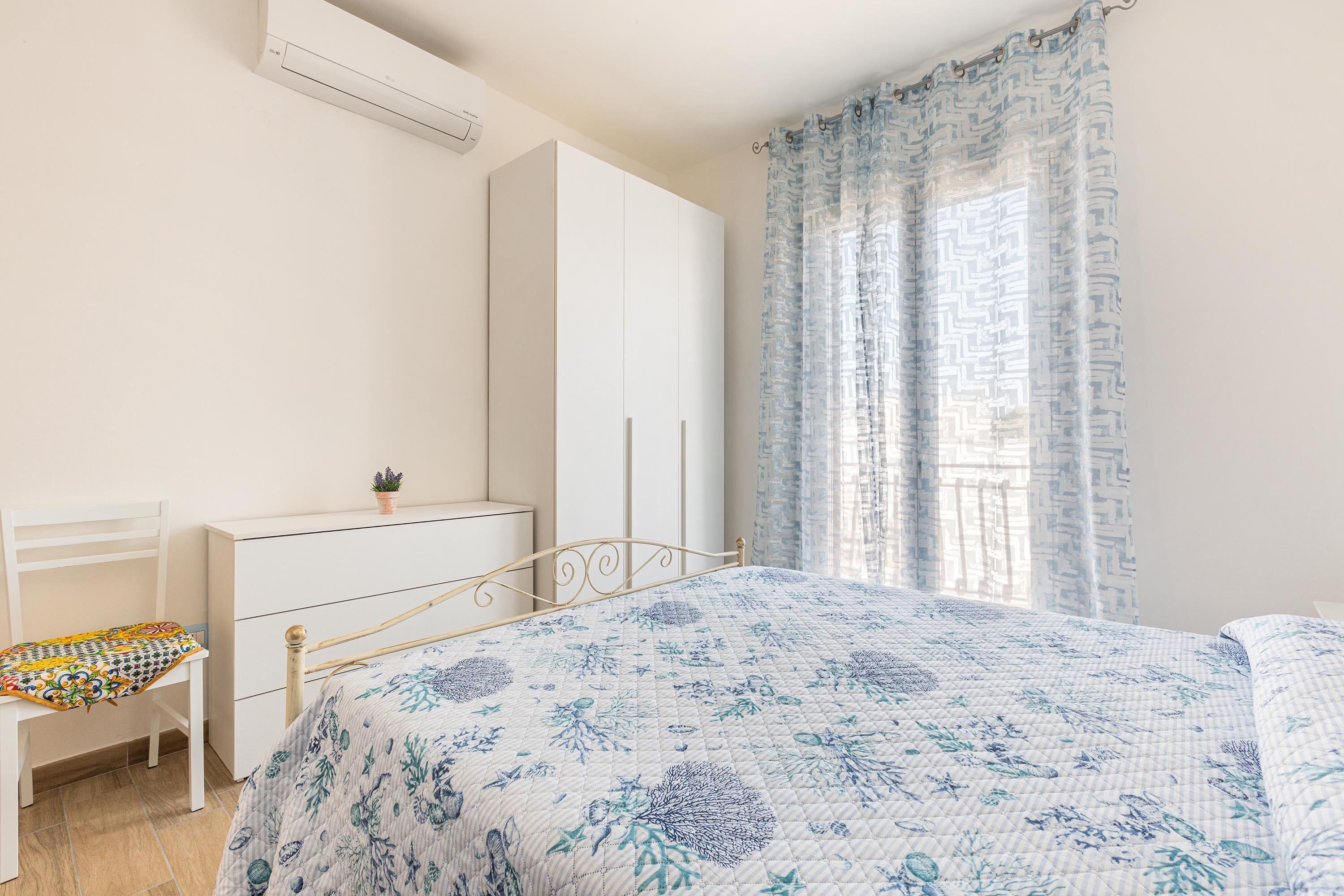 A bedroom with a bed, a chair, a dresser, and a window with curtains.