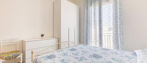 Une chambre à coucher avec un lit, une chaise, une commode et une fenêtre avec des rideaux.