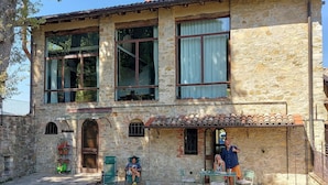 Ein Gebäude aus Stein mit großen Fenstern, einer überdachten Terrasse und Sitzgelegenheiten im Freien.