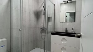 A modern bathroom with a glass-enclosed shower, a toilet, a sink with a mirror, and a vanity with drawers.