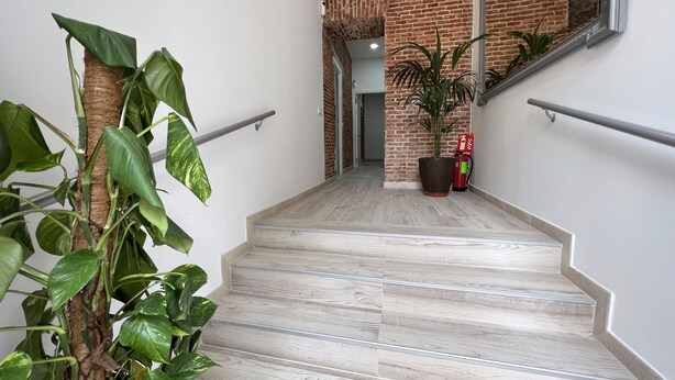 A staircase with a modern design, leading to a room with a brick wall and a large mirror.