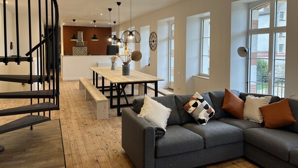 A modern living room with a grey sofa, wooden flooring, a dining area with a wooden table, and a spiral staircase. - Former high-capacity factory in the heart of Chagny (Chagny)