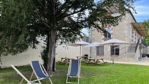 A grassy outdoor area with two lounge chairs, picnic tables, and umbrellas. A stone building with a staircase is in the background. - Former high-capacity factory in the heart of Chagny (Chagny)