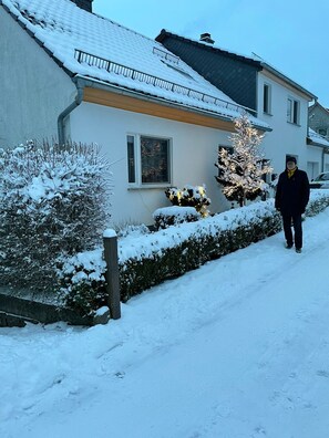 Un edificio residencial con techo nevado y una persona caminando por un sendero cubierto de nieve.