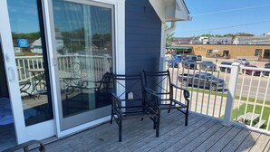 Een houten terras met twee stoelen, een bank en een schuifdeur naar een buitenruimte met een patio tafel en stoelen.