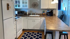 Een moderne keuken met witte kasten, een magnetron, een spoelbak en een klok aan de muur.