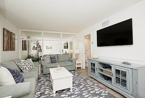A modern living room with a grey sofa, white coffee table, and a flat-screen TV mounted on the wall.