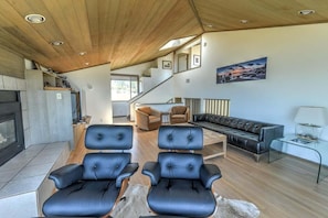A modern living room with a fireplace, leather sofas, and a staircase leading to an upper level. - Sea Break | Coastal Escape with Hot Tub (Sea Ranch)