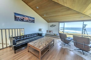 A modern living room with a leather sofa, a wooden coffee table, and a view of the ocean through large windows. - Sea Break | Coastal Escape with Hot Tub (Sea Ranch)