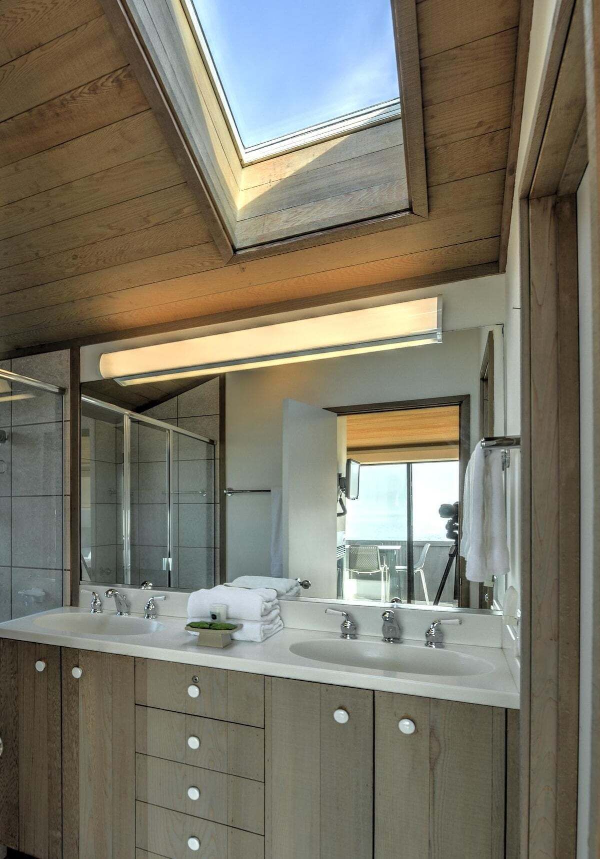 A modern bathroom with a skylight, dual sinks, and a large mirror.