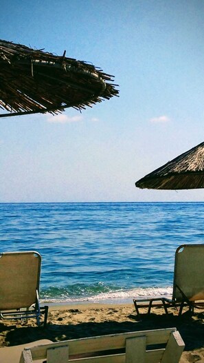 A beach with two lounge chairs and thatched umbrellas, overlooking the sea. - Stylish apartment in a wellness oasis 300 meters from the beach (Nea Mesangala)
