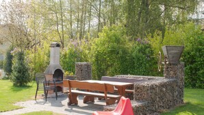 Eine Terrasse im Freien mit einem Grillbereich aus Stein, einer hölzernen Bank und einem roten Kunststoffstuhl.