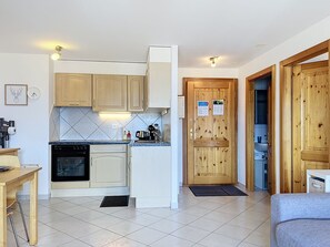 A compact kitchen with a built-in oven, wooden cabinets, and a tiled backsplash. - Grand Panorama A5 by Interhome (Nendaz)