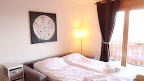 Et hotelværelse med seng, skrivebord, lampe og et vindue med gardiner.