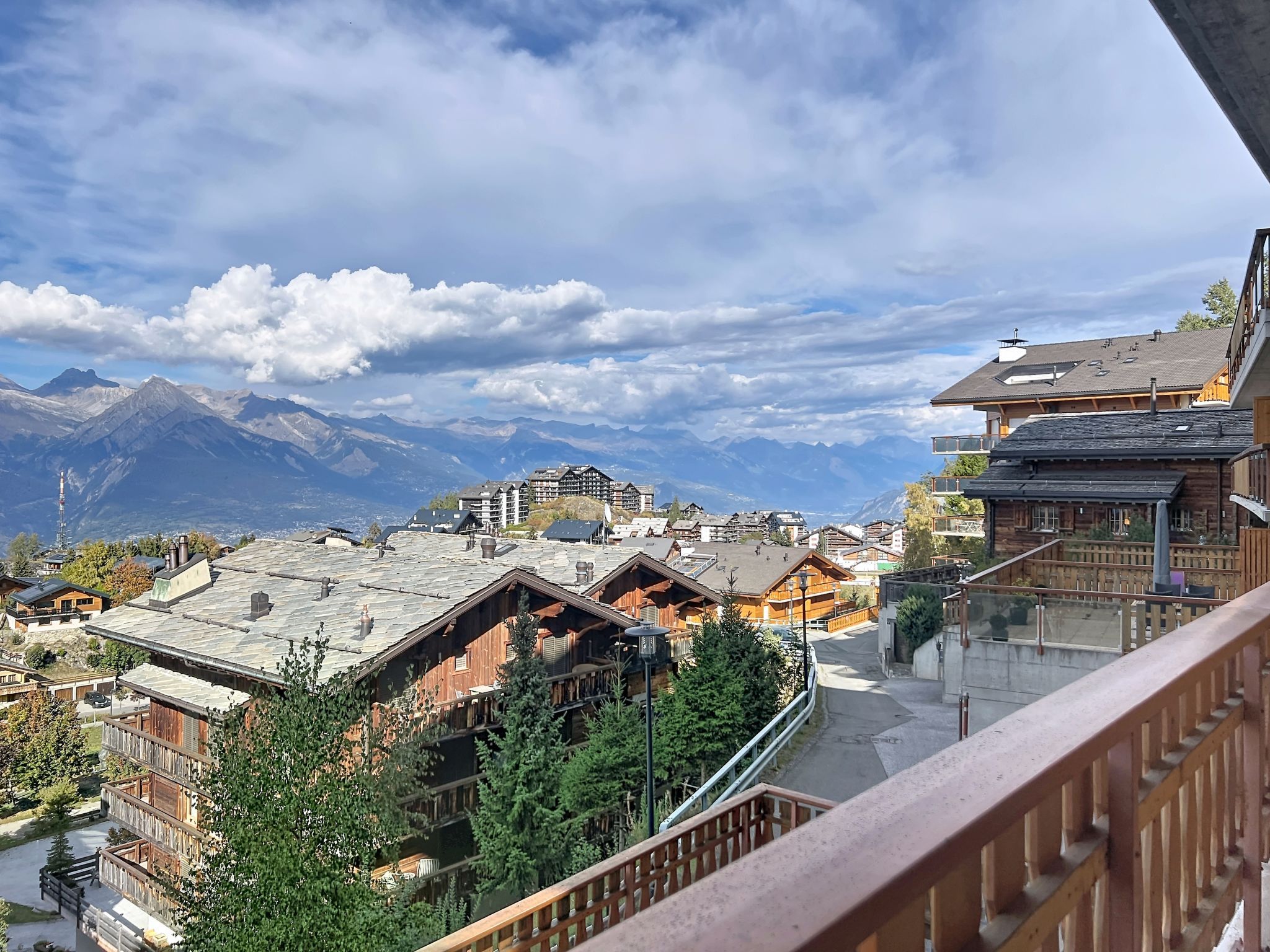 A mountain village with traditional wooden buildings, a clear sky, and snow-capped mountains in the background.