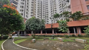 A residential building with multiple balconies, a landscaped garden with a central tree, and a paved walkway. - Transit ID (Depok)