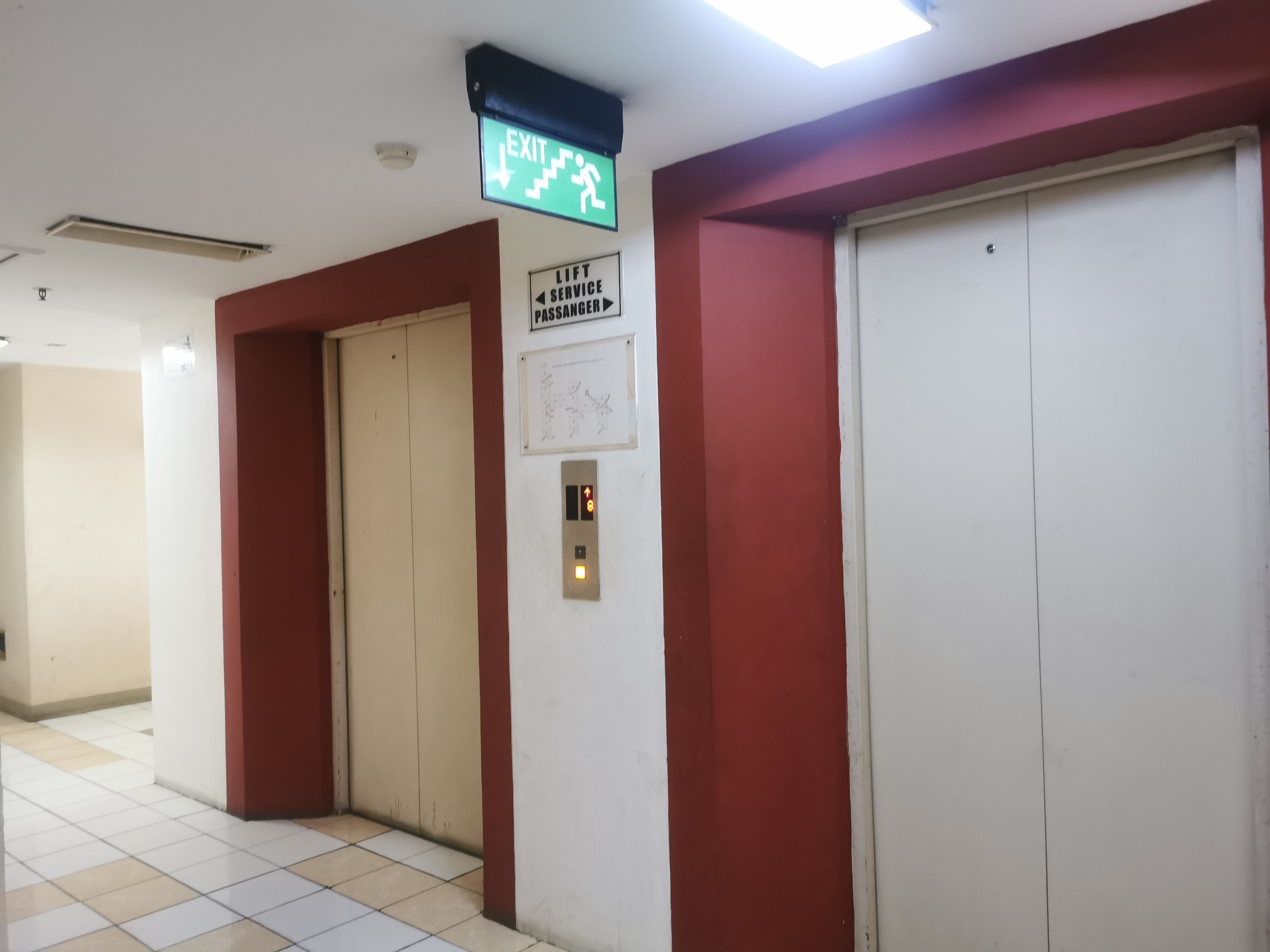 An elevator area with a green exit sign, a lift service passenger sign, and a lift control panel.