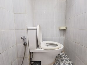 Um pequeno banheiro revestido com azulejos, com vaso sanitário, secador de mãos e chuveiro.