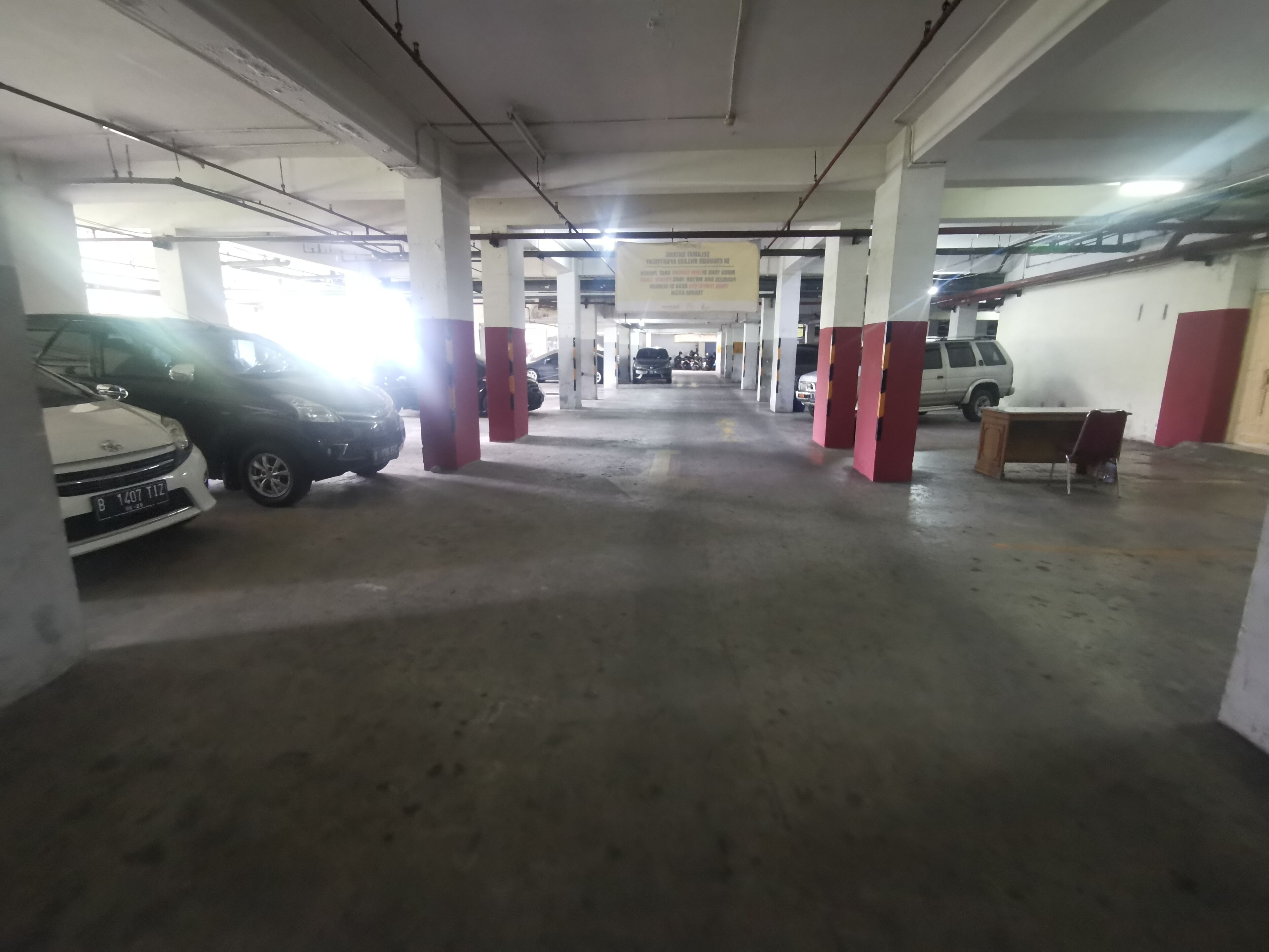 An indoor parking garage with concrete pillars, a few parked cars, and a bench.