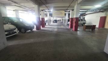 An indoor parking garage with concrete pillars, a few parked cars, and a bench.