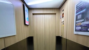 An elevator interior with a wooden door, a digital display, and a poster advertising internet speeds. - Transit ID (Depok)