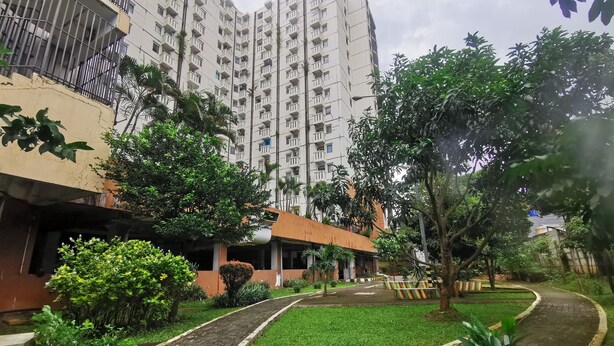 A residential building with multiple balconies, a well-maintained garden with a brick pathway, and a variety of greenery. - Transit ID (Depok)