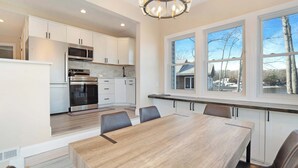 Une cuisine moderne avec des meubles blancs, des appareils en acier inoxydable et une grande table à manger avec des chaises.
