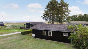 A black building with a sloped roof, a large tree in front, and a grassy area with a path leading to it. - Awesome home in ørsted with WiFi (Ørsted)