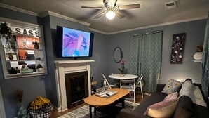A living room with a fireplace, a ceiling fan, a television, and a dining area. - {Bunga-YOLO} Fun and Games in CLT's Best Neighborhood. Hot Tub NEW and working! (Charlotte)