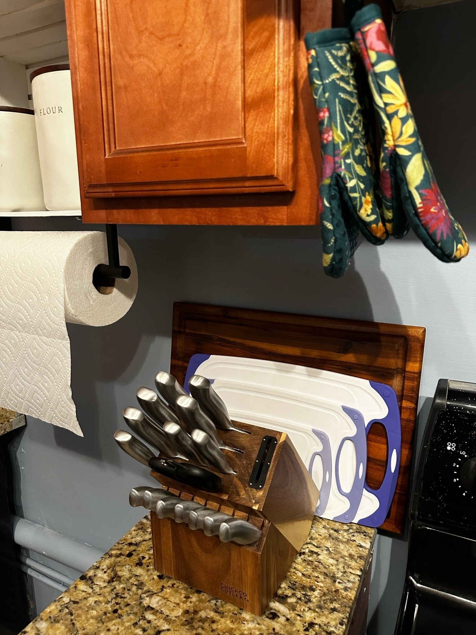 A kitchen counter with a knife block, a roll of paper towels, and a wooden cabinet above.