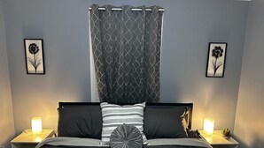 A bedroom with a bed, two bedside tables with lamps, a patterned curtain, and two wall-mounted flower art pieces. - {Bunga-YOLO} Fun and Games in CLT's Best Neighborhood. Hot Tub NEW and working! (Charlotte)