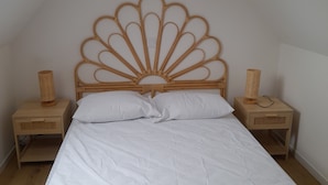 Un dormitorio con cabecera de madera, ropa de cama blanca, dos mesitas de noche con lámparas y techo inclinado.