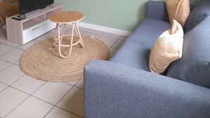 Una sala de estar con una escalera de madera, un televisor sobre un mueble de madera, un sofá gris con cojines y una alfombra redonda de fibras naturales.