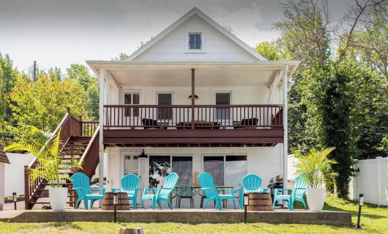 A two-story house with a balcony, outdoor seating area with chairs, and a staircase leading to the upper floor.
