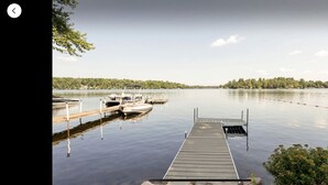 A calm lake with a wooden dock extending into the water, surrounded by trees and a distant shoreline.