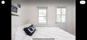 Une chambre à coucher avec un lit, deux fenêtres, une porte et un luminaire fixé au mur.