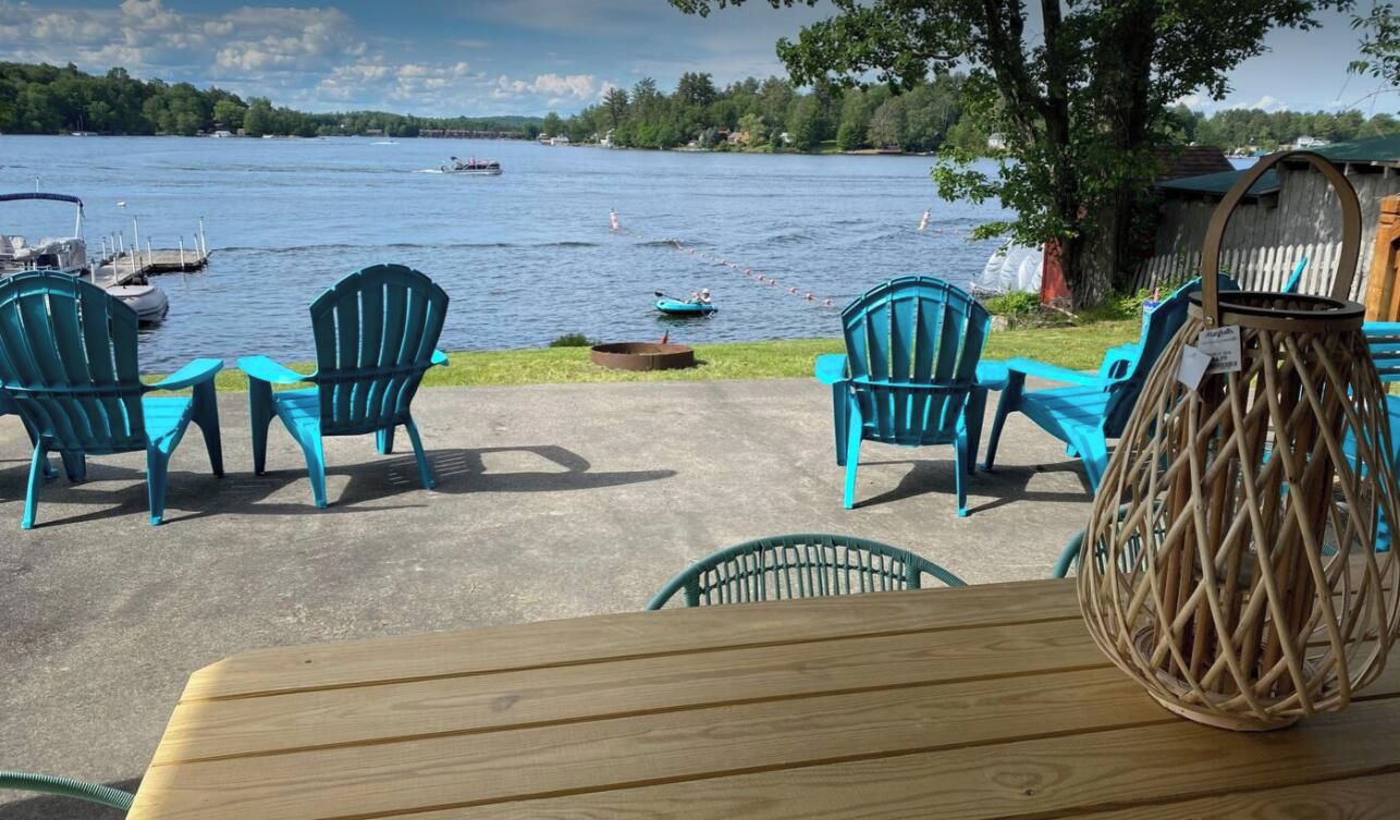 Un espacio al aire libre con sillas y una mesa, con vistas a un lago con barcos.