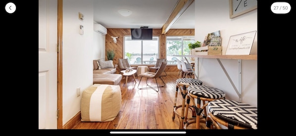 Un salon moderne avec un plancher en bois, un canapé, une table basse et un espace détente comprenant des fauteuils et des poufs.