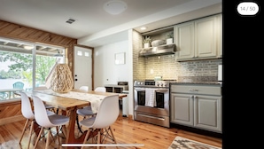 A modern kitchen with a wooden dining table, white chairs, and a brick backsplash.