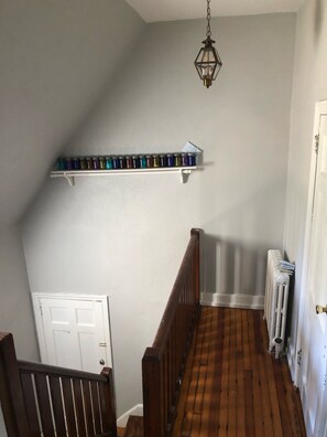 Un pasillo con una escalera de madera, un radiador y una estantería con frascos.