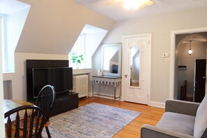 Un espace de vie compact comprenant un téléviseur, un coin repas, un canapé et une petite table.