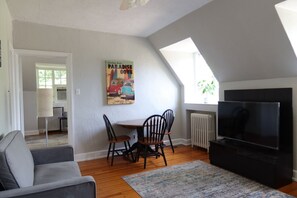 Una sala de estar con televisor, una mesa de comedor con sillas, un sofá y un cuadro en la pared.