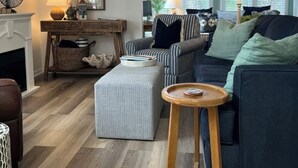 A living room with a fireplace, striped sofa, ottoman, and a small wooden table. - Boutique Beachside condo with easy access to beach (St. Augustine)