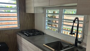 Une cuisine compacte équipée d’une cuisinière à gaz, d’un évier et d’une fenêtre donnant sur une terrasse en bois.